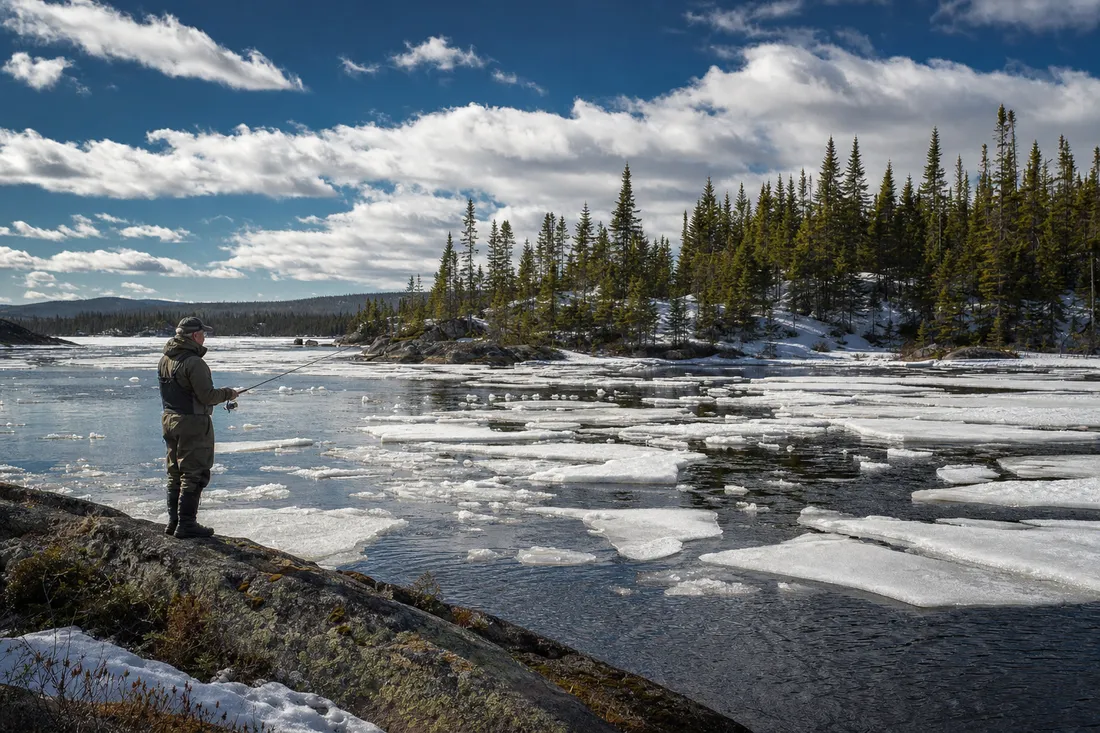 Angler casting from a rocky point as ice sheets break up on a northern Québec lake in spring
